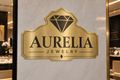 Brushed gold ACP logo Aurelia Jewelry on marble wall with stand-offs
